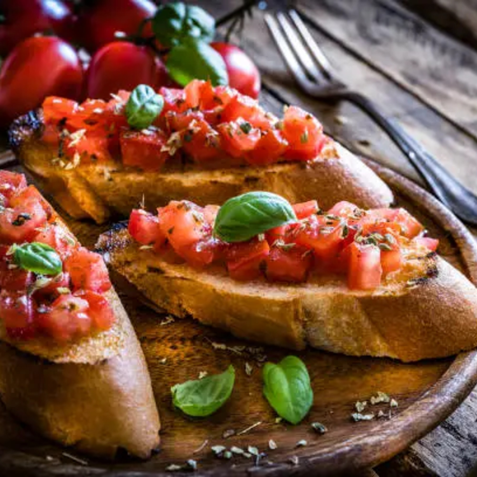 Three bruschetta slices with diced tomatoes, basil, and seasoning on a wooden board.