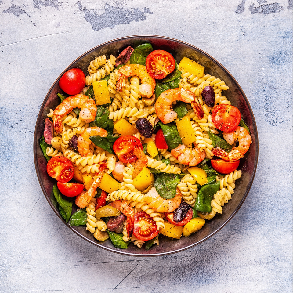 A vibrant bowl of Italian fusilli pasta salad with shrimp, tomatoes, spinach, and bell peppers.