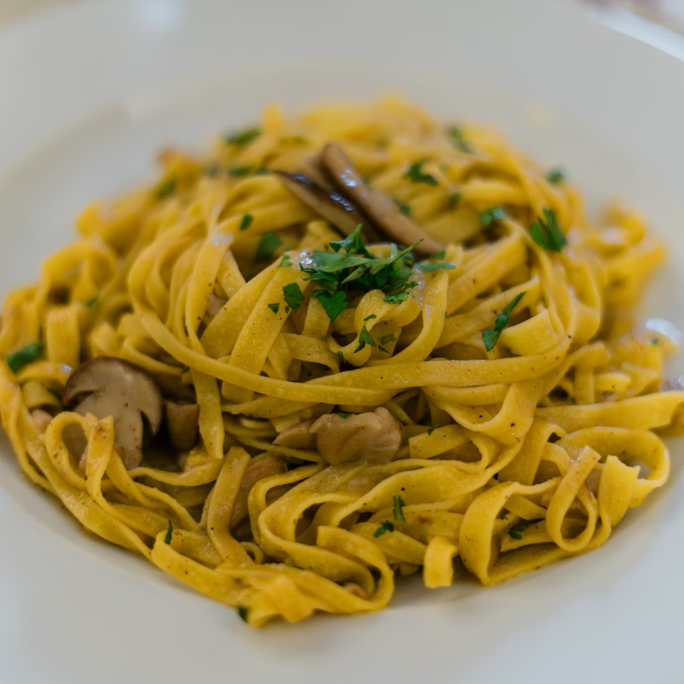 Close-up of Julius Ristorante's tagliatelle pasta with mushrooms and parsley on a white plate.