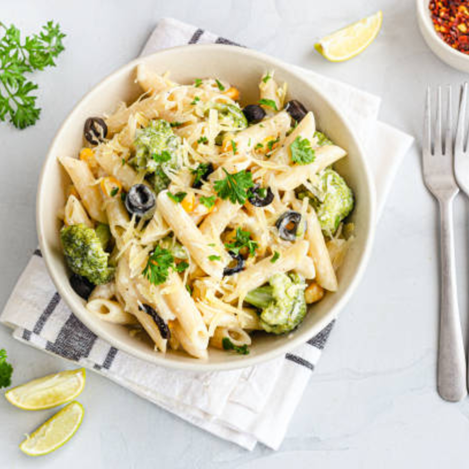 Creamy penne pasta with broccoli, black olives, corn, and parsley, served with lime and chili flakes.