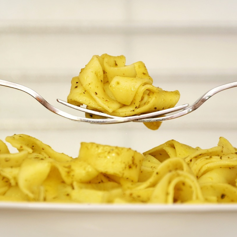 Fork lifting a swirl of pappardelle pasta with pesto sauce from a white plate.