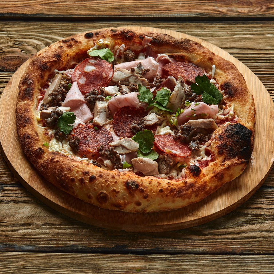 A Julius Ristorante pizza with pepperoni, ham, ground meat, mushrooms, and fresh herbs on a wooden board.
